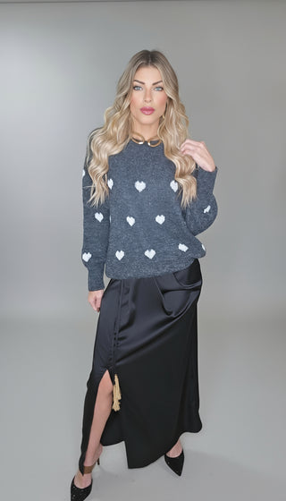 Woman wearing a dark blue sweater with white heart patterns and a black skirt indoors.